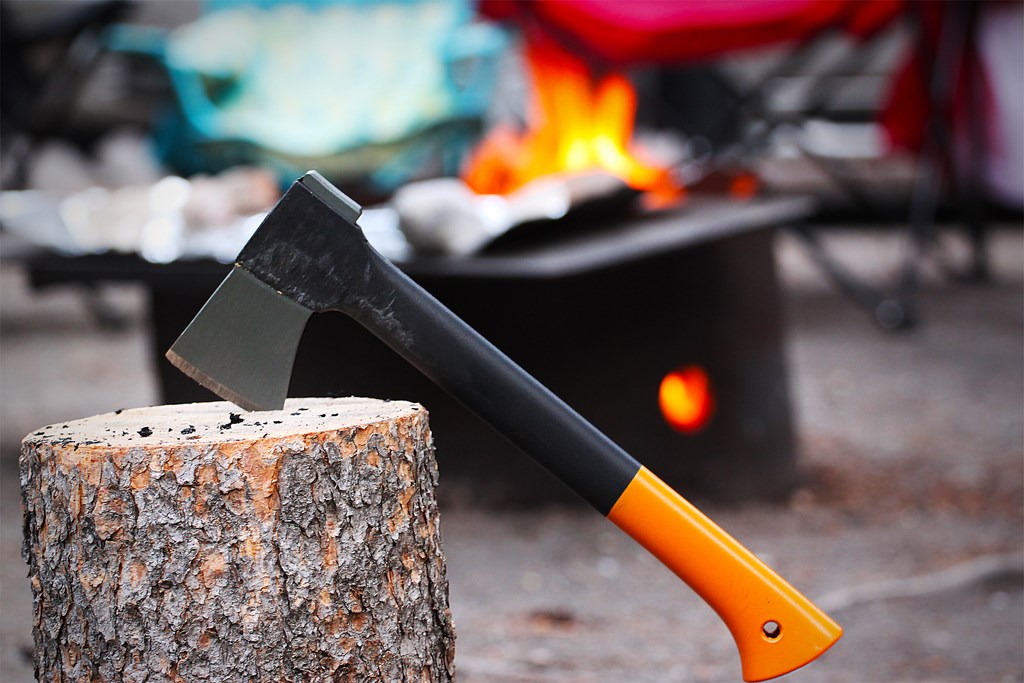 Axe stuck in a stump with a campfire burning in the background.