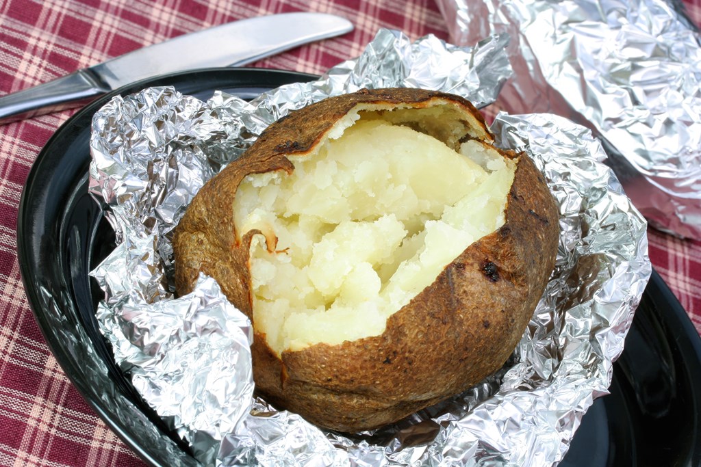 One fresh baked potato, open on aluminum foil.