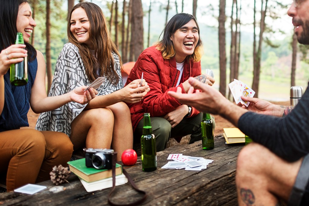 A group of friends laughing and playing cards while camping.