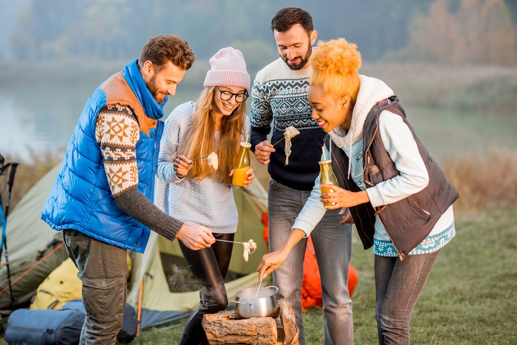 Group of four friends sharing a pot of fondue while tent camping.