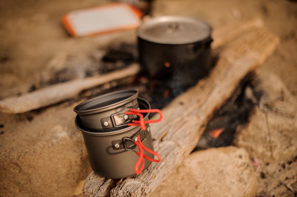 Set of metal camping pots and pans on a wood background.