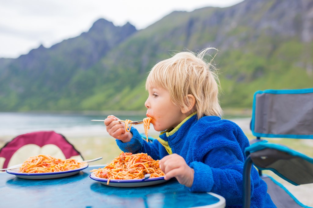 A child eating spaghetti at a campsite.