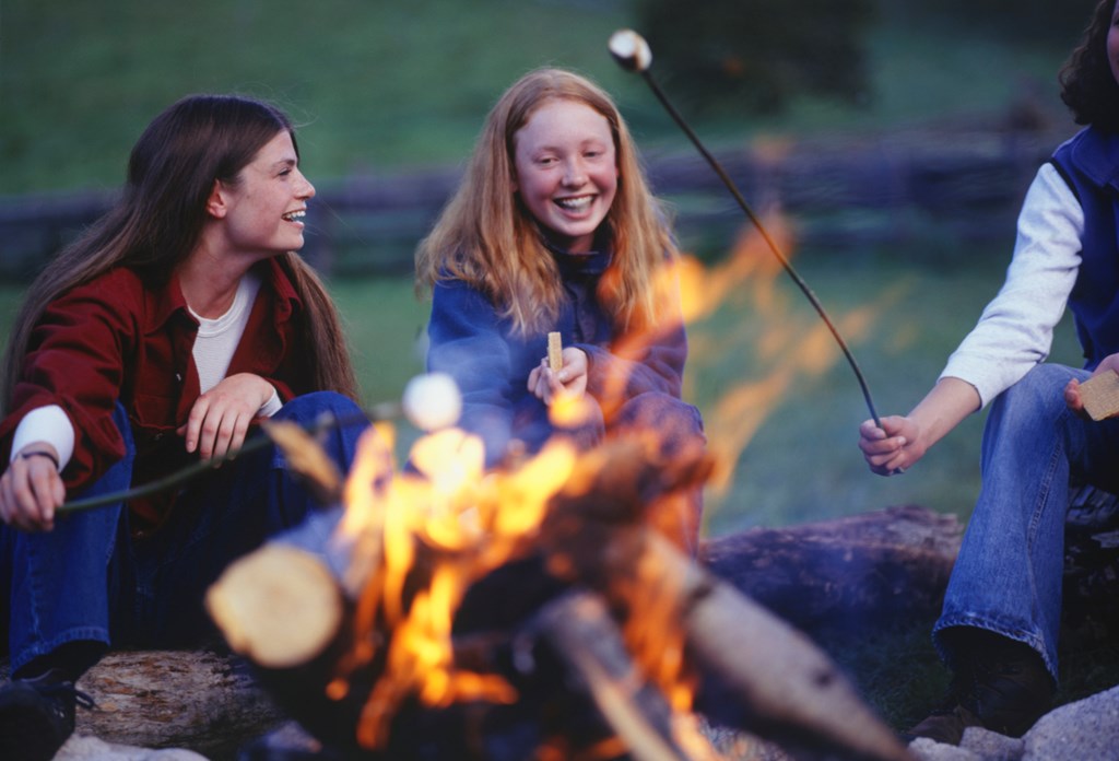 Teenage girls laugh around the campfire while roasting marshmallows to help introduce this short spooky story for kids
