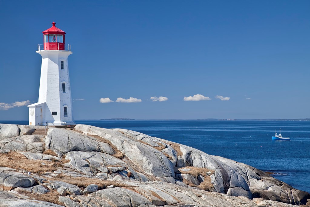 Peggy's Cove lighthouse, one of the major tourism destinations in Nova Scotia, Canada.  Lobster boat gathering traps in the background.