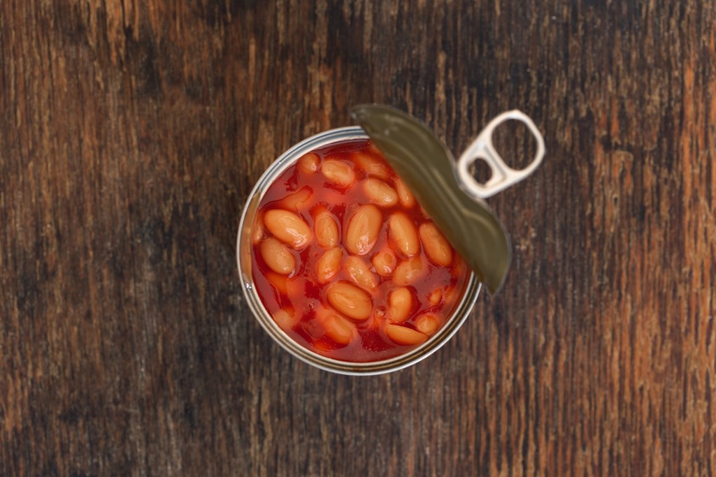 Canned beans in a tin on wooden background, top view.