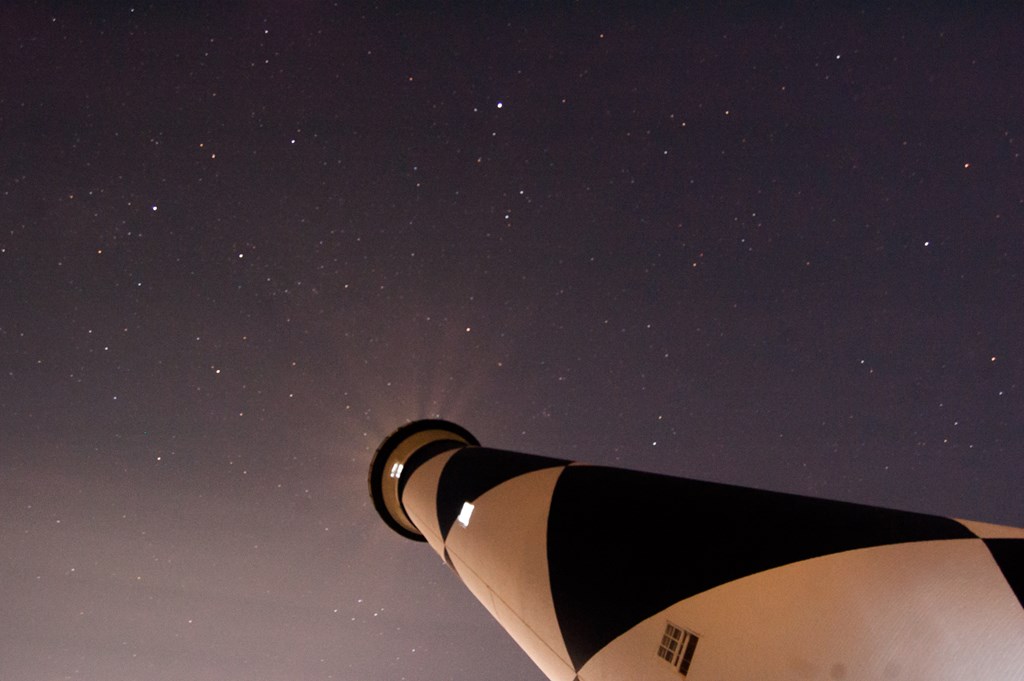 Looking upward at a black and white lighthouse with the stars shinning at night.
