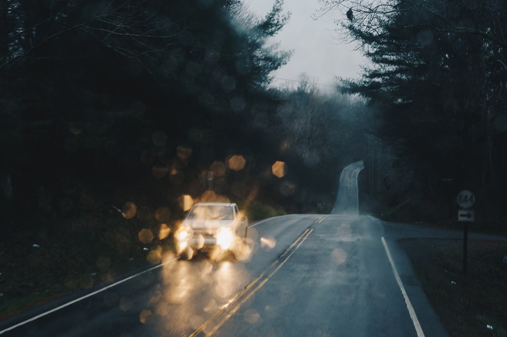 View of a vehicle and rainy road from the windshield of a car.