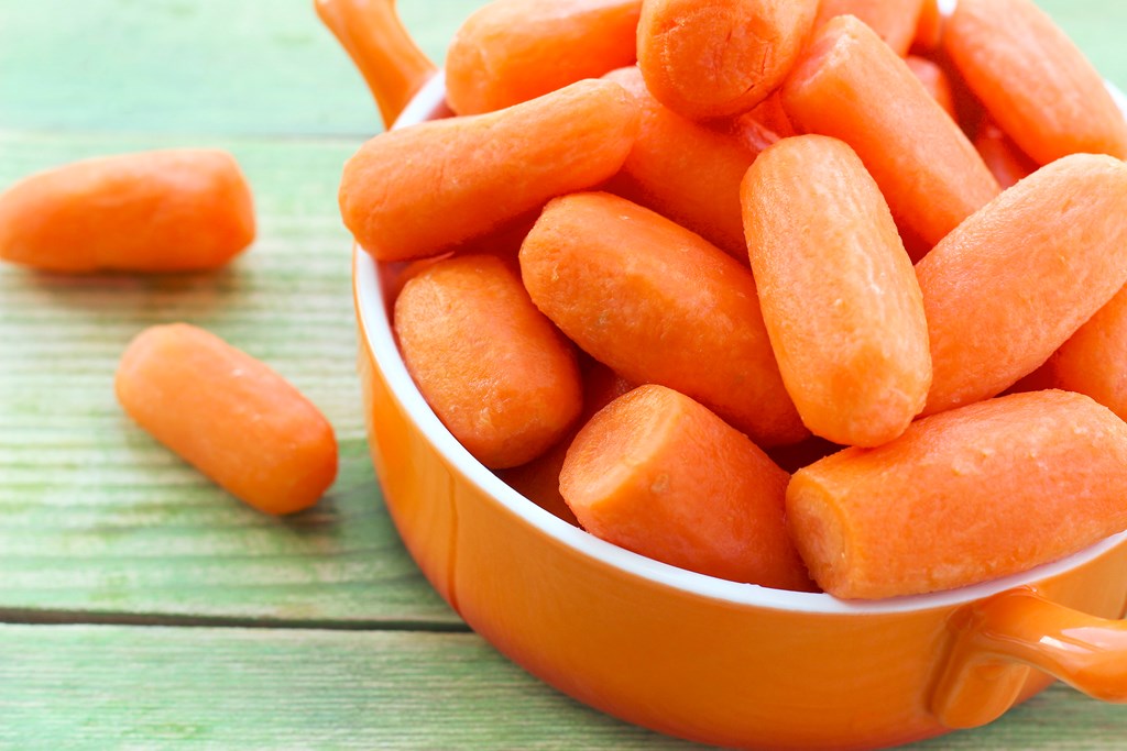 Small baby carrots in orange ceramic bowl on a green wooden background.