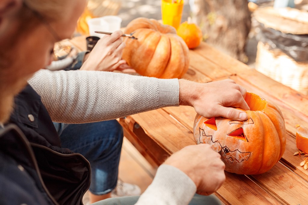 Cropped view of young adult man and woman carving pumpkins outside on a crisp fall day.
