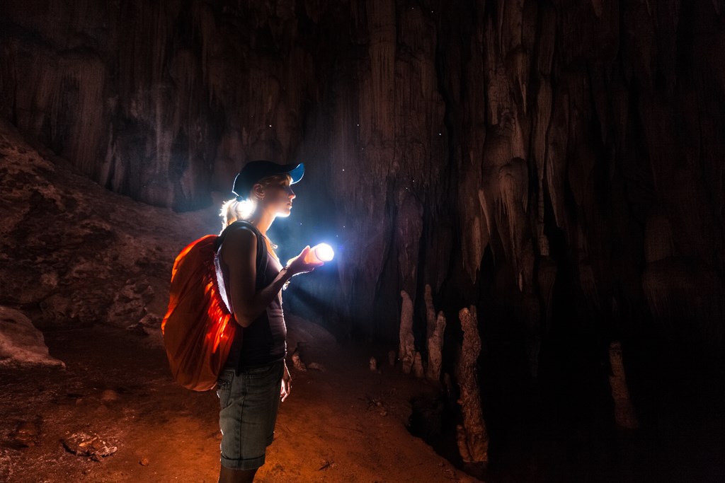 Young woman explores the cave with a flashlight.