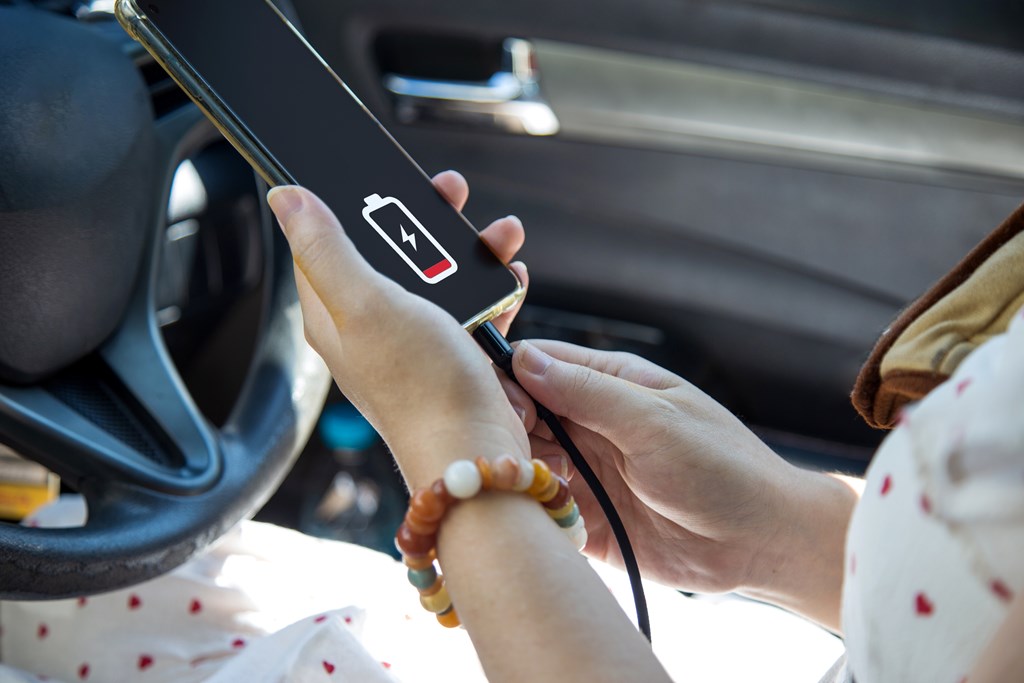 Close up a woman in a white dress charging her mobile phone with car charger cable.