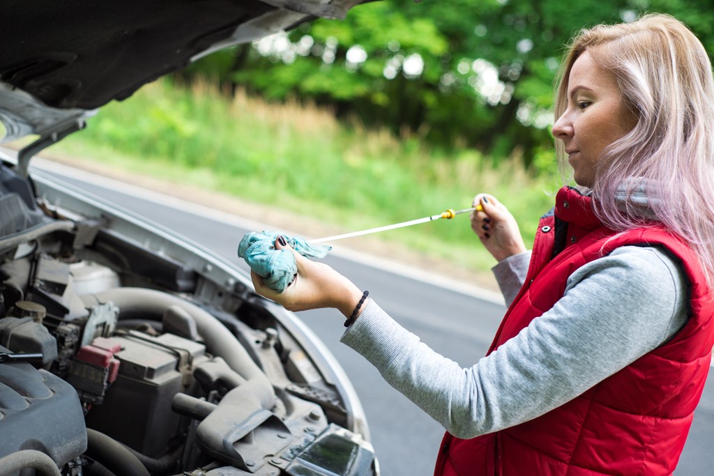 Woman checks the oil level from her car's engine.