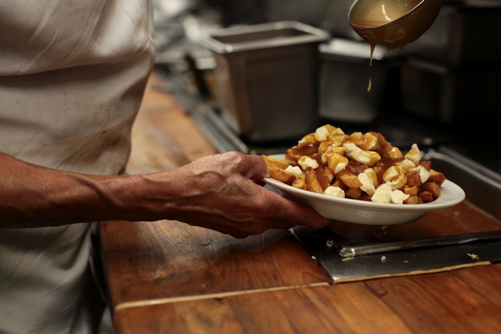 Close-up of a chef adding gravy to Poutine. French fries, cheese curds and gravy.