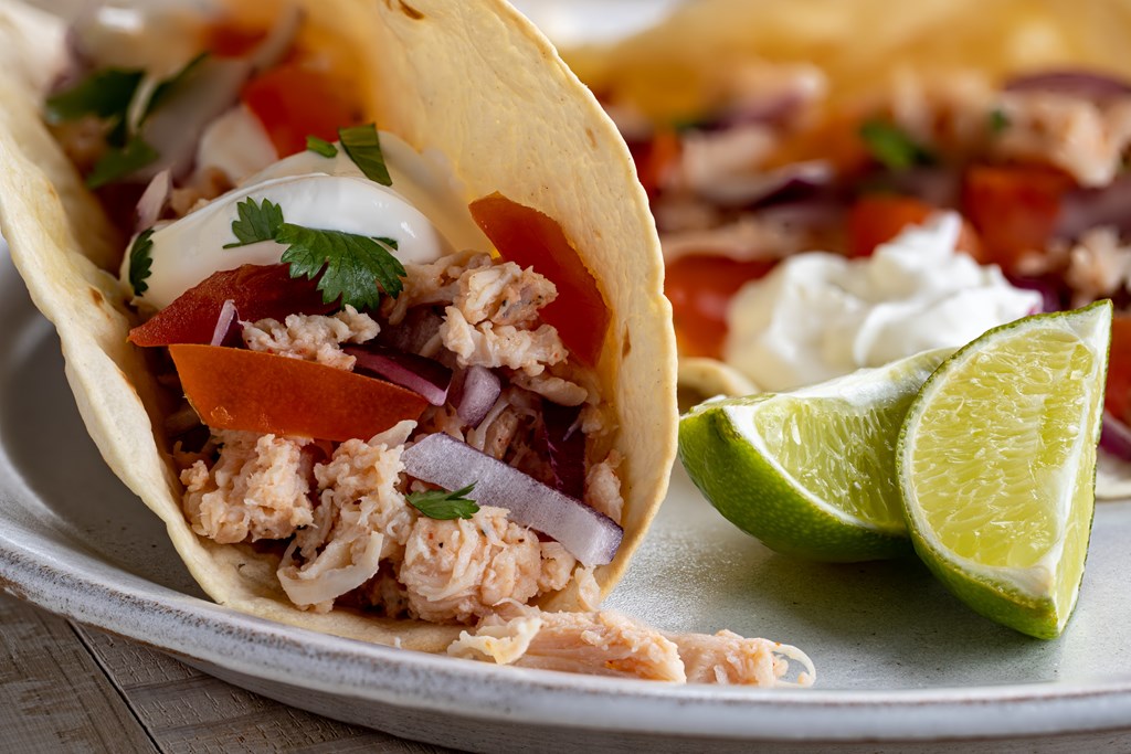 Closeup of a taco with pulled chicken, tomato, onion and sour cream on a plate with lime wedges