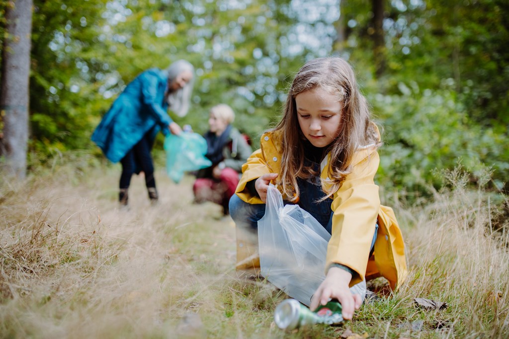A small girl with mother and grandmother picking up waste outdoors.