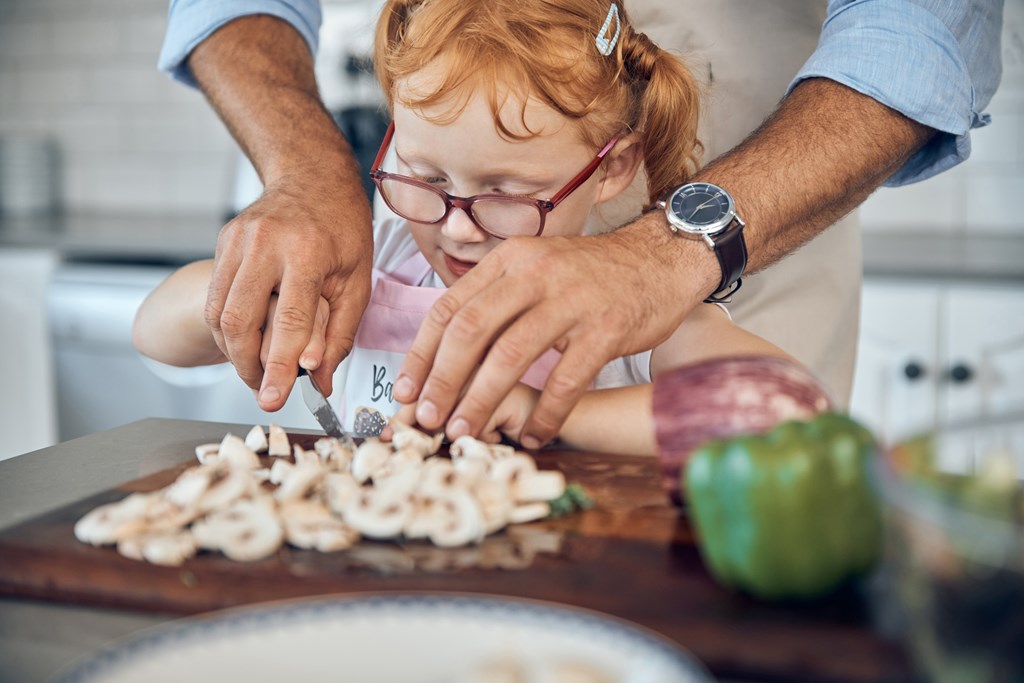 Child cutting mushrooms with the help of her father.