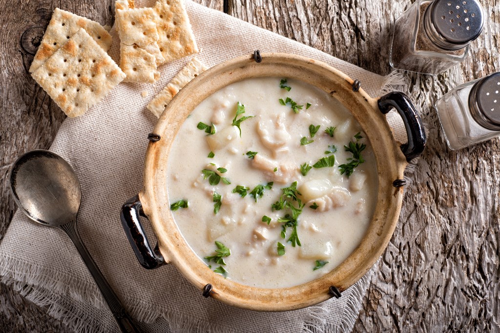 A delicious creamy white fish chowder with haddock, cod, potato, and onion garnished with parsley and served with soda crackers.