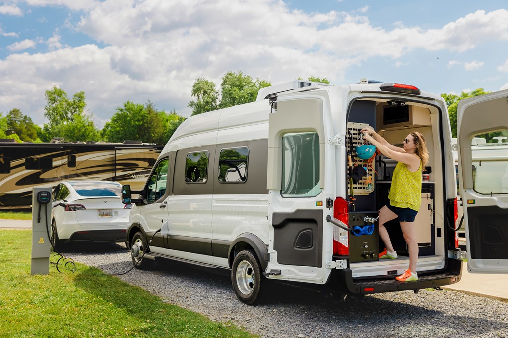 Woman unpacking the back of an electric RV at a KOA campground.