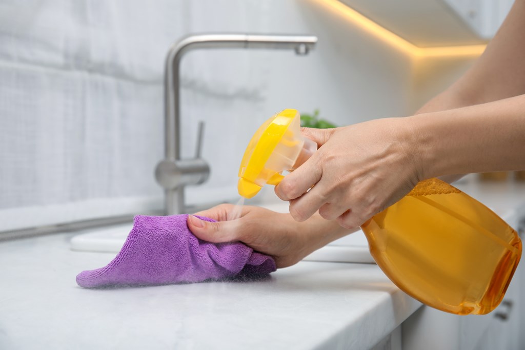 Woman cleaning white marble countertop with rag and spray.