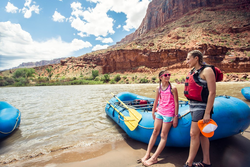 Smiling child and adult women ready to board a large inflatable raft as they travel down the scenic Colorado River.