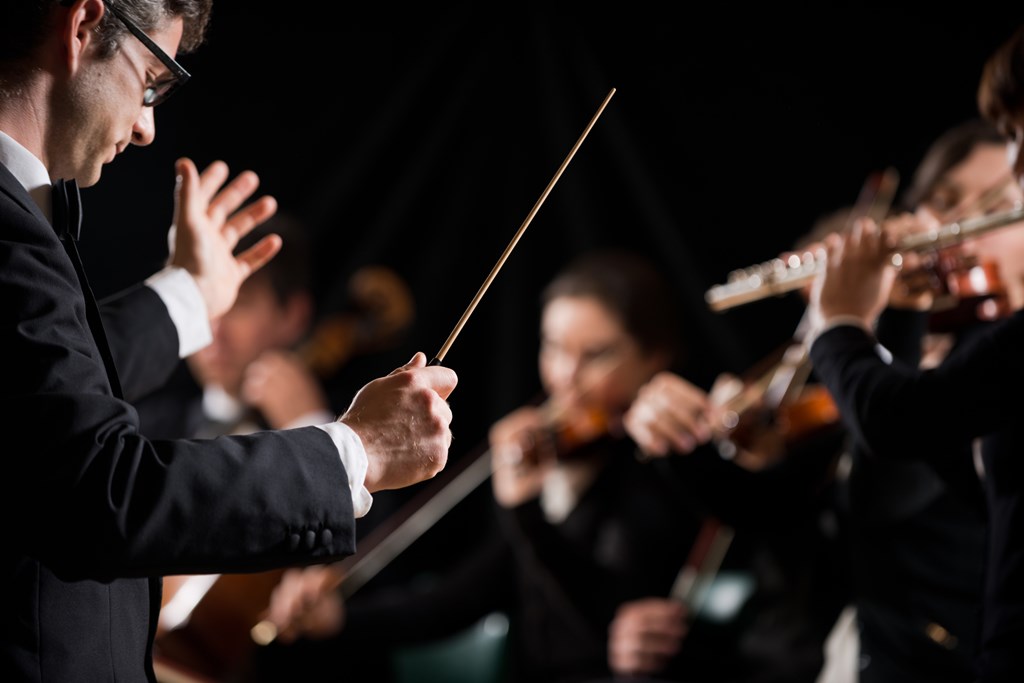 Conductor directing symphony orchestra with performers on background.