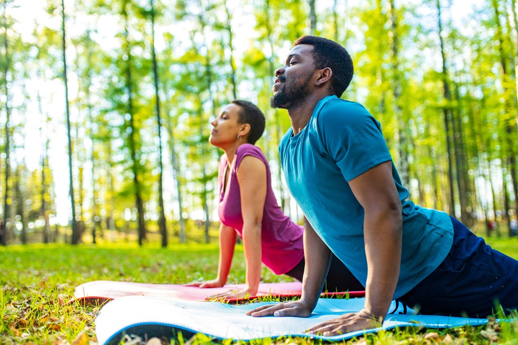 A young woman and man doing yoga in green forest.