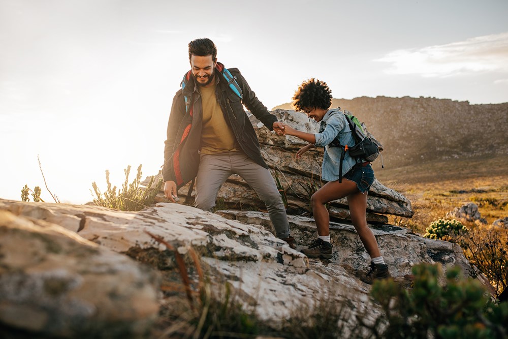 Young man helping friend to climb up the rock.