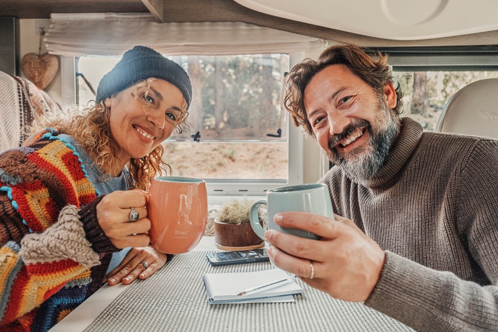 A couple raises their mugs at the small table inside their RV.