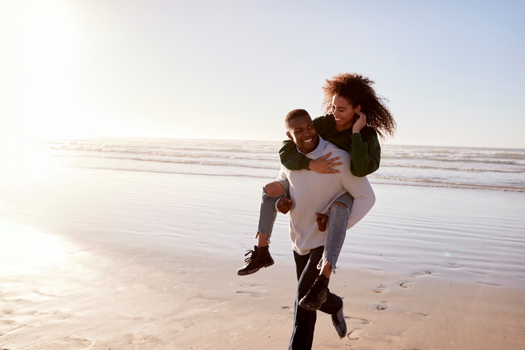 Man giving a woman a piggyback ride on the beach during a winter holiday.