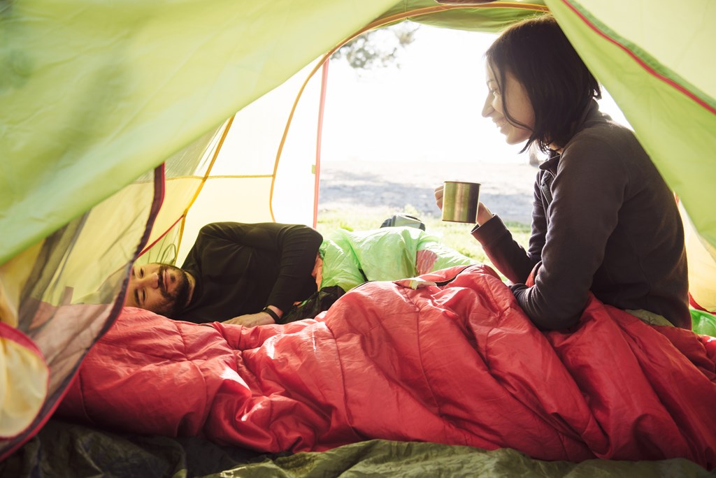 Two friend traveling and spending time in tent while drinking coffee in the morning. 