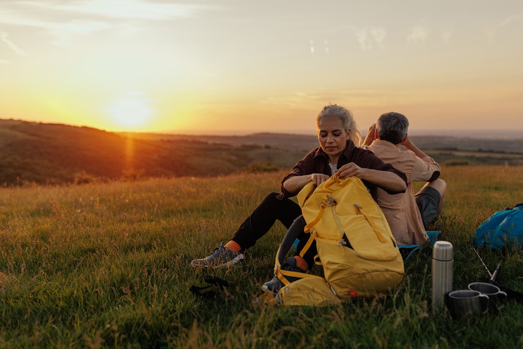 A middle aged couple is packing their backpacks and checking the route for a day of hiking.