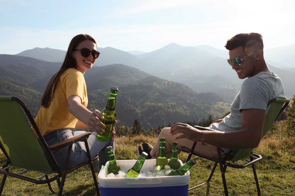 Couple enjoys cold drinks from a cooler on a mountaintop.