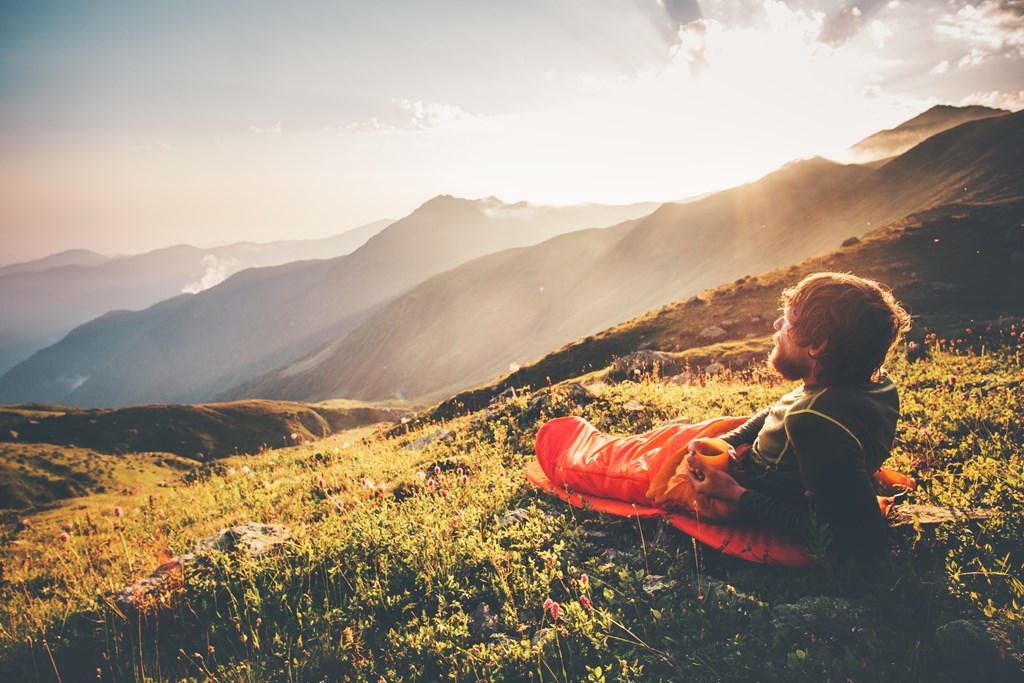 Man cowboy camping - camping with just a sleeping bag - in a beautiful, misty mountain backdrop.