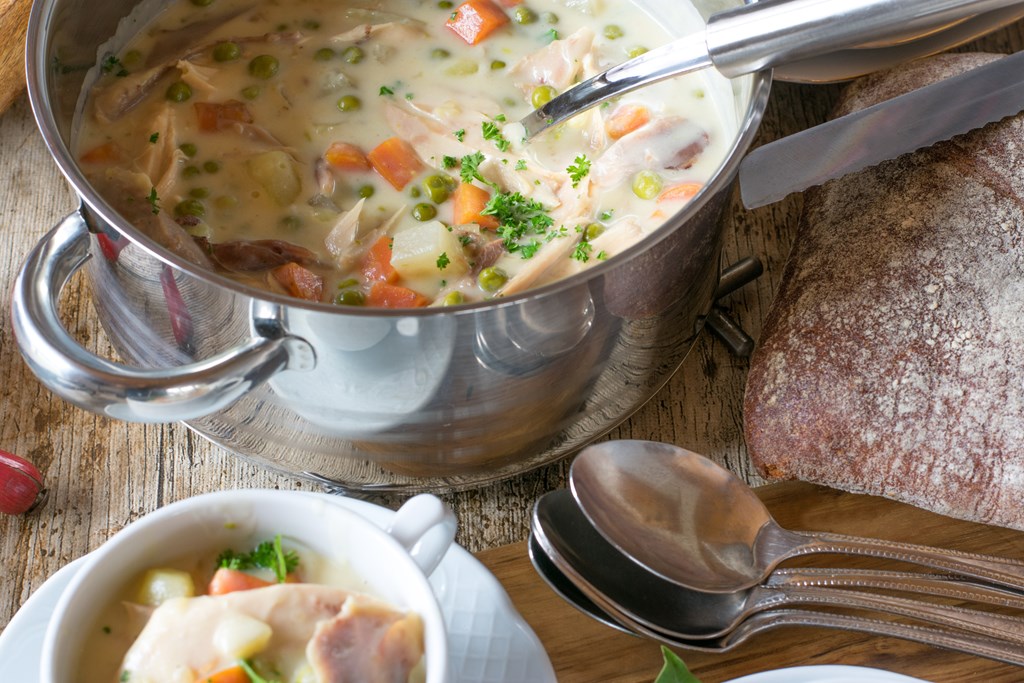 homemade and fresh cooked chicken cream soup with vegetables and chicken meat served in soup pot on a table with spoons