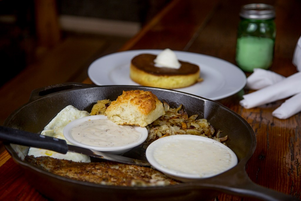 A southern breakfast spread including steak, hashbrowns, biscuit and gravy served in a cast iron skillet. 