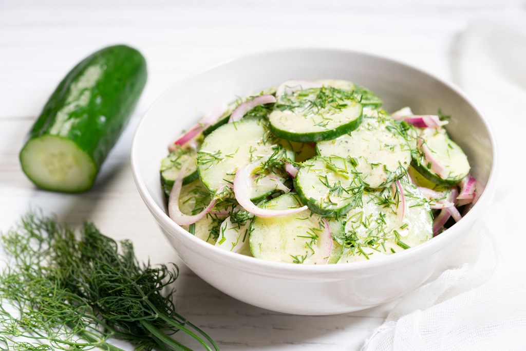 Cucumber and red onion salad on white wooden background.
