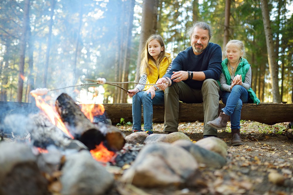 Sisters and their father roasting marshmallows.