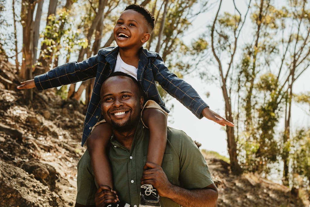 Cute boy sitting on his father's shoulders on a forest trail. 