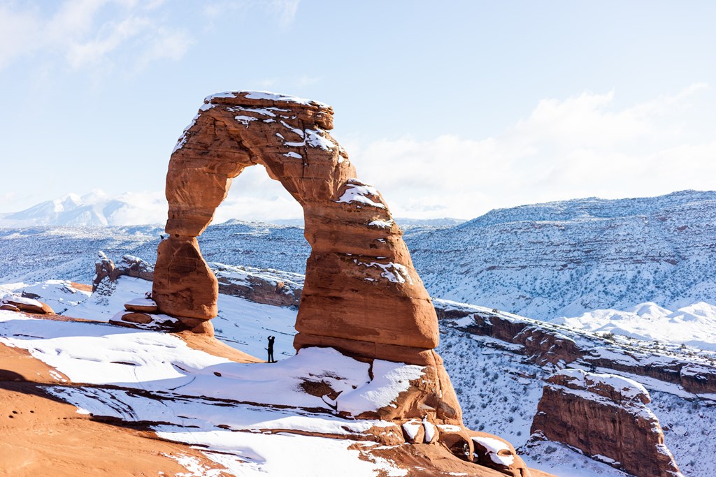 Man standing beneath famous Delicate Arch at Arches National Park Utah in the winter.