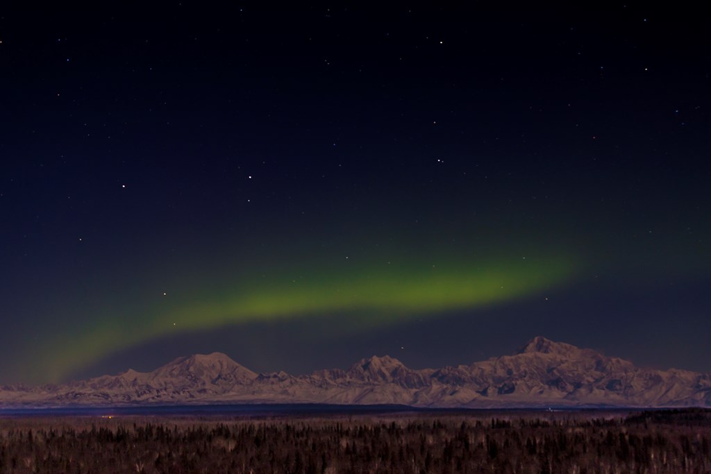 The aurora borealis (northern lights) above the Alaska Range in central Alaska. From left to right, the mountains are Mt. Foraker, Mt. Hunter and Mt. McKinley (Denali.)