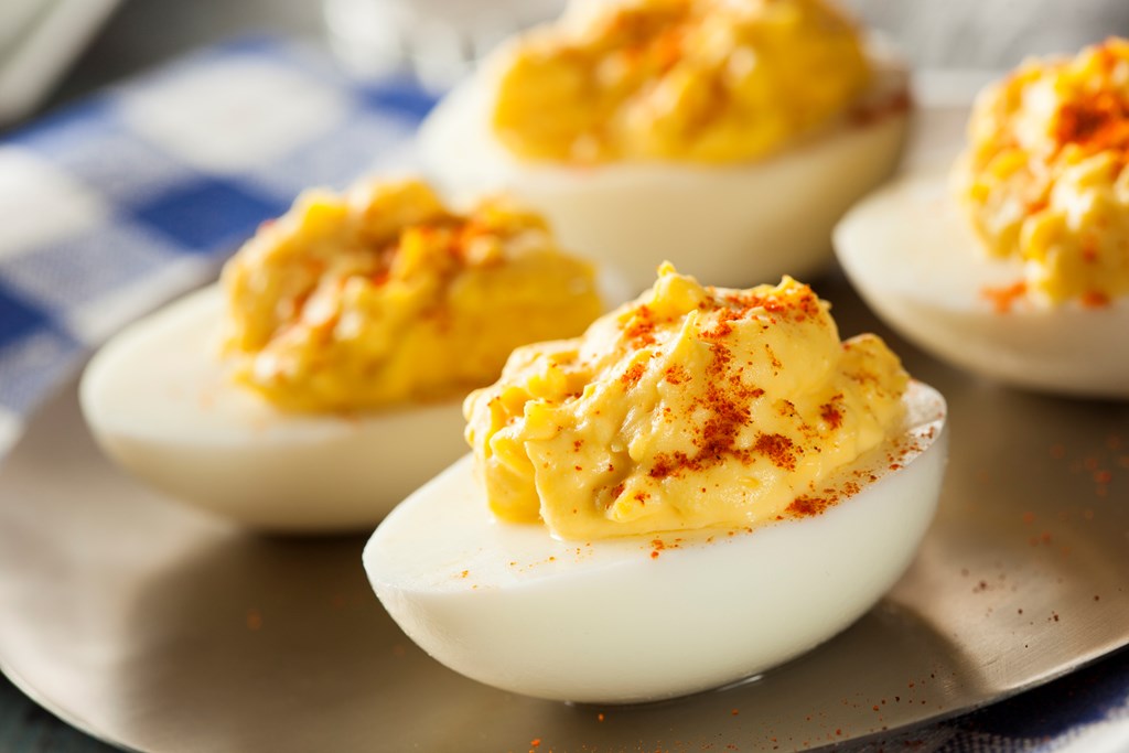 A closeup of four devilled eggs on a plate against a blue gingham backdrop.