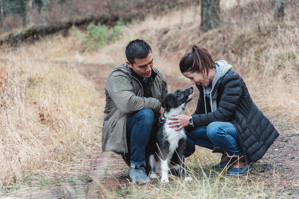A couple crouching down with their dog on a trail.