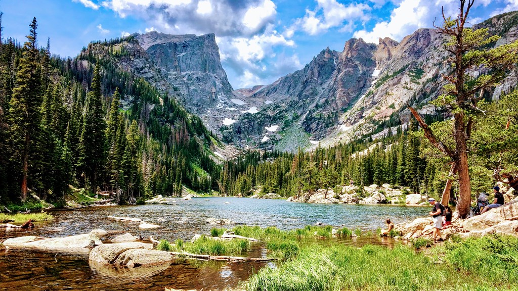 Hikers pause at the edge of a gorgeous mountain lake on a sunny day in Rocky Mountain National Park.
