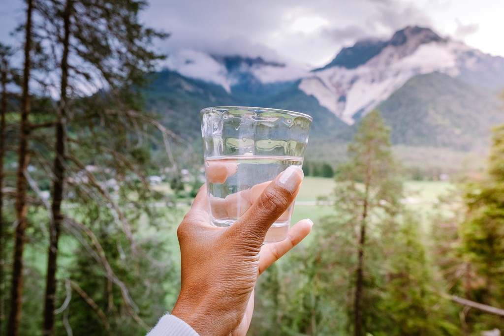 Glass of water in hand looking out over mountains.`