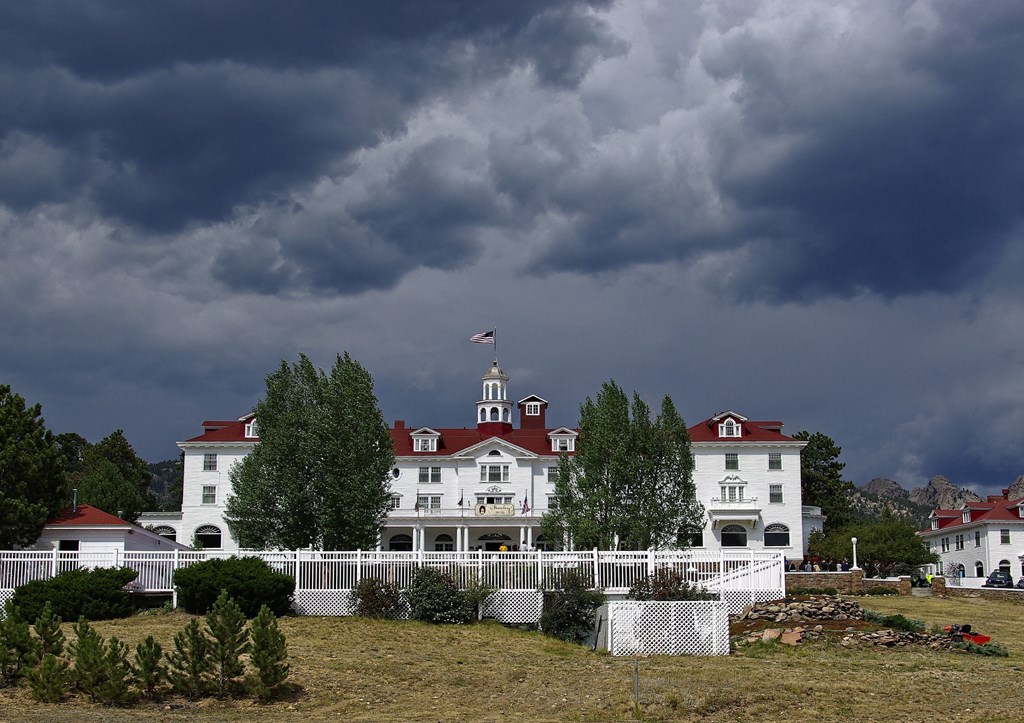 The Stanley Hotel in Estes Park Colorado during a storm. Large, white hotel with red roof on a backdrop of dark storm clouds.