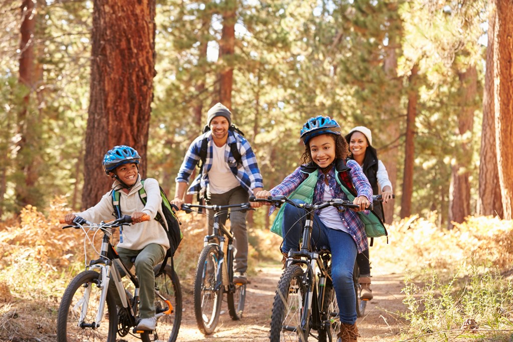 Two parents and young kids mountain bike through a fall forest.