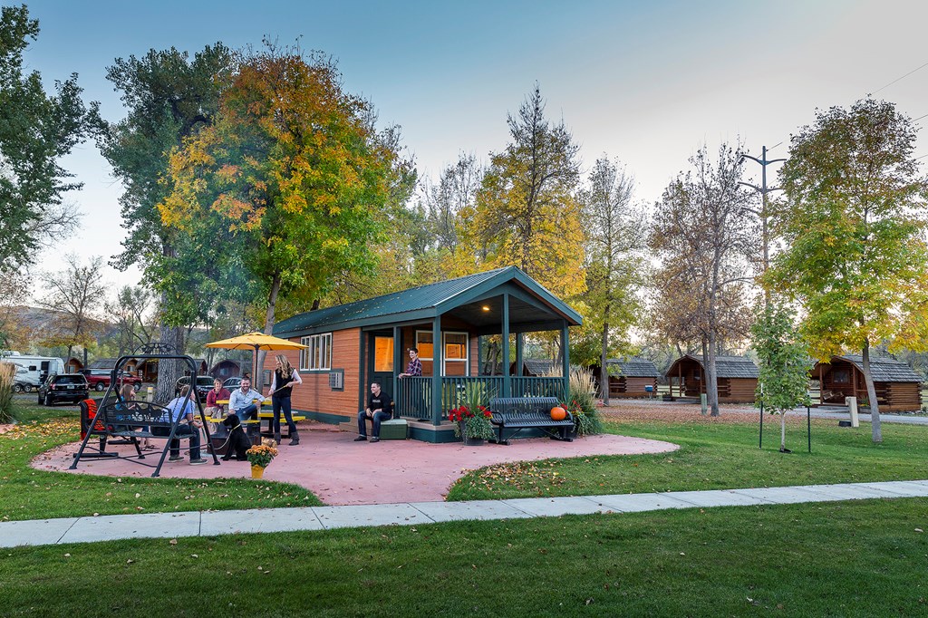 A cozy cabin sits in front of colorful trees during a fall evening at a KOA campground.