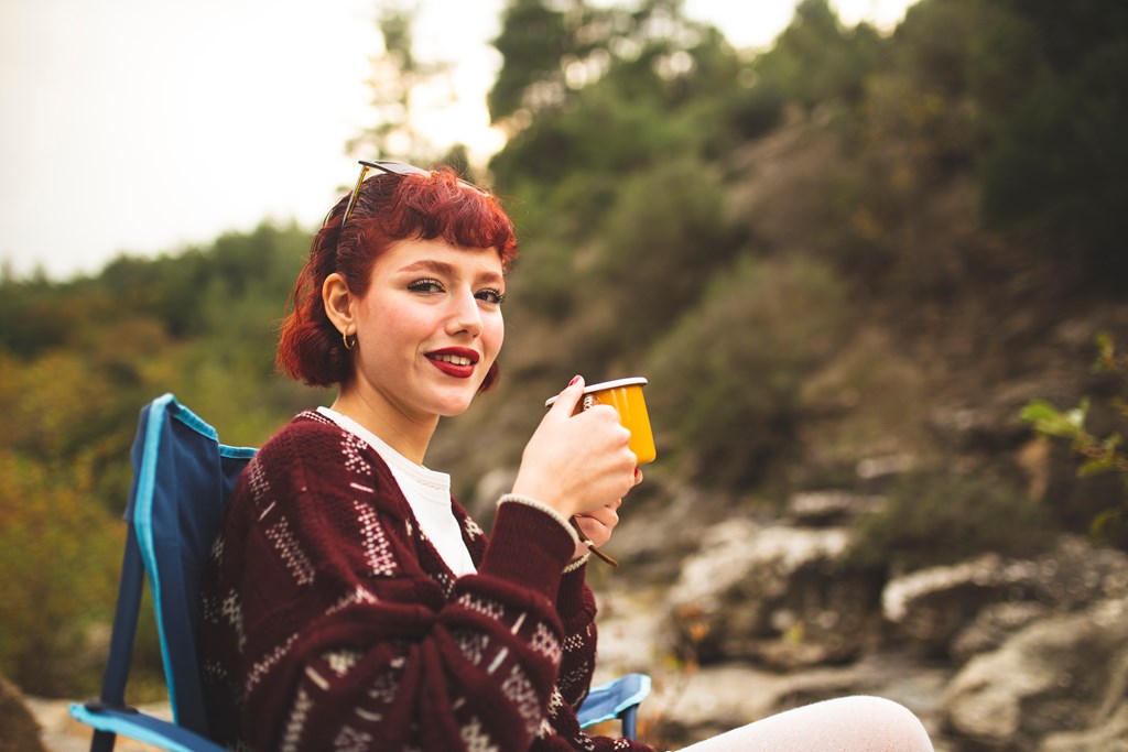 Young woman drinking coffee at her campsite on a fall day.