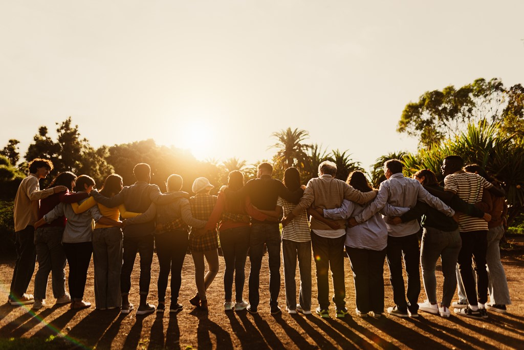 Back view of happy multigenerational people arm in arm in the sunset.