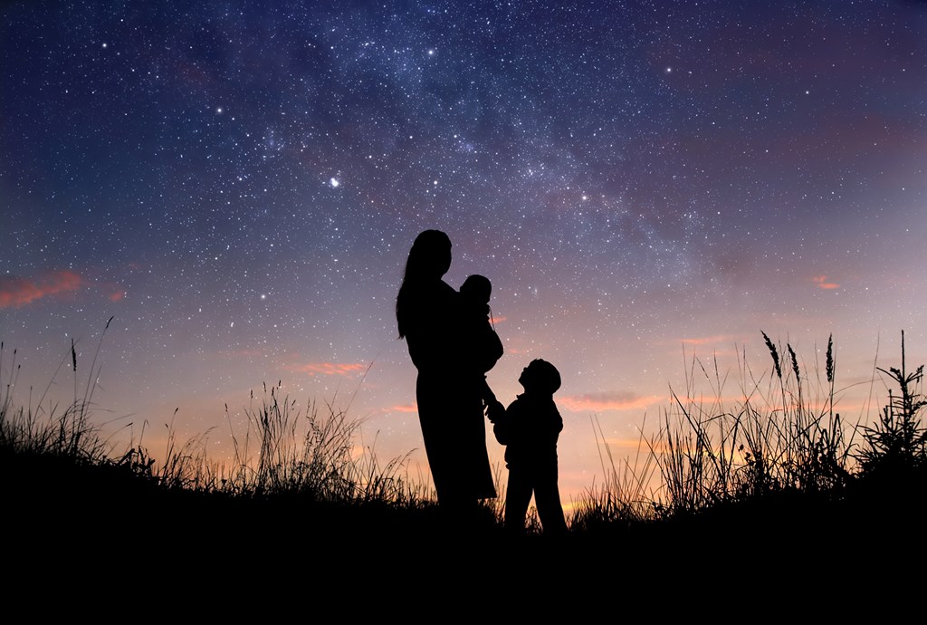 Silhouette of mother and her two little children against starry night sky